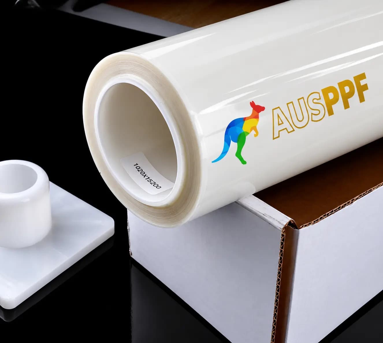 A roll of AusPPF Clear 7.5 paint protection film, printed with the AusPPF logo, resting on its retail box.