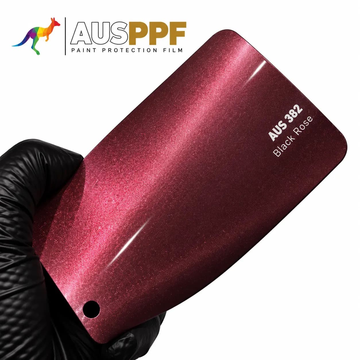 A gloved hand holding a swatch of AusPPF AUS-382 Black Rose PPF, showing its gloss finish.