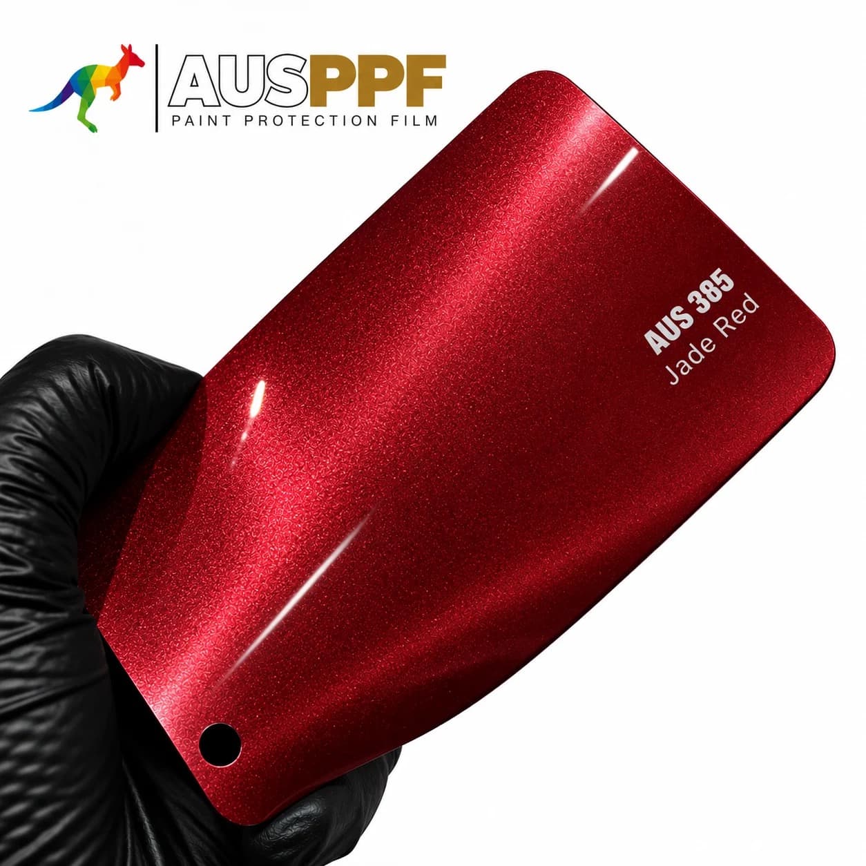 A gloved hand holding a swatch of AusPPF AUS-385 Jade Red PPF, showing its gloss finish.