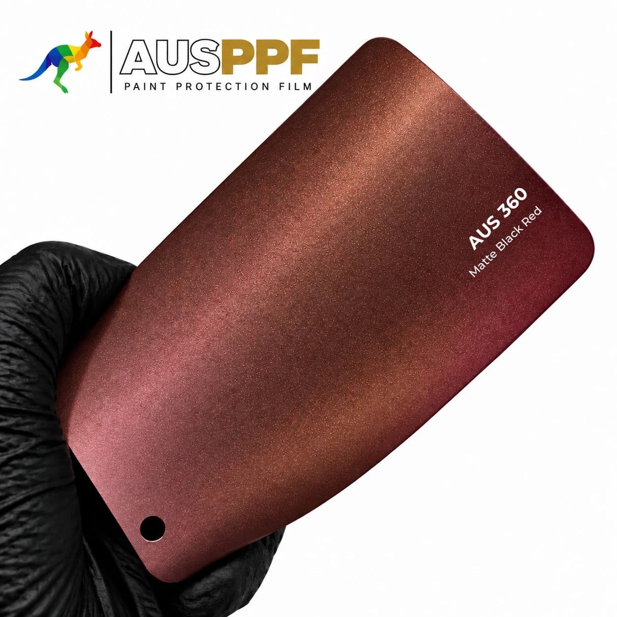A gloved hand holding a swatch of AusPPF AUS-360 Matte Black Red PPF, showing its matte finish.
