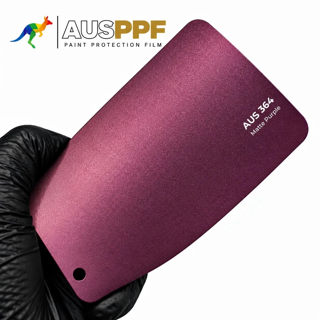 A gloved hand holding a swatch of AusPPF AUS-364 Matte Purple PPF, showing its matte finish.