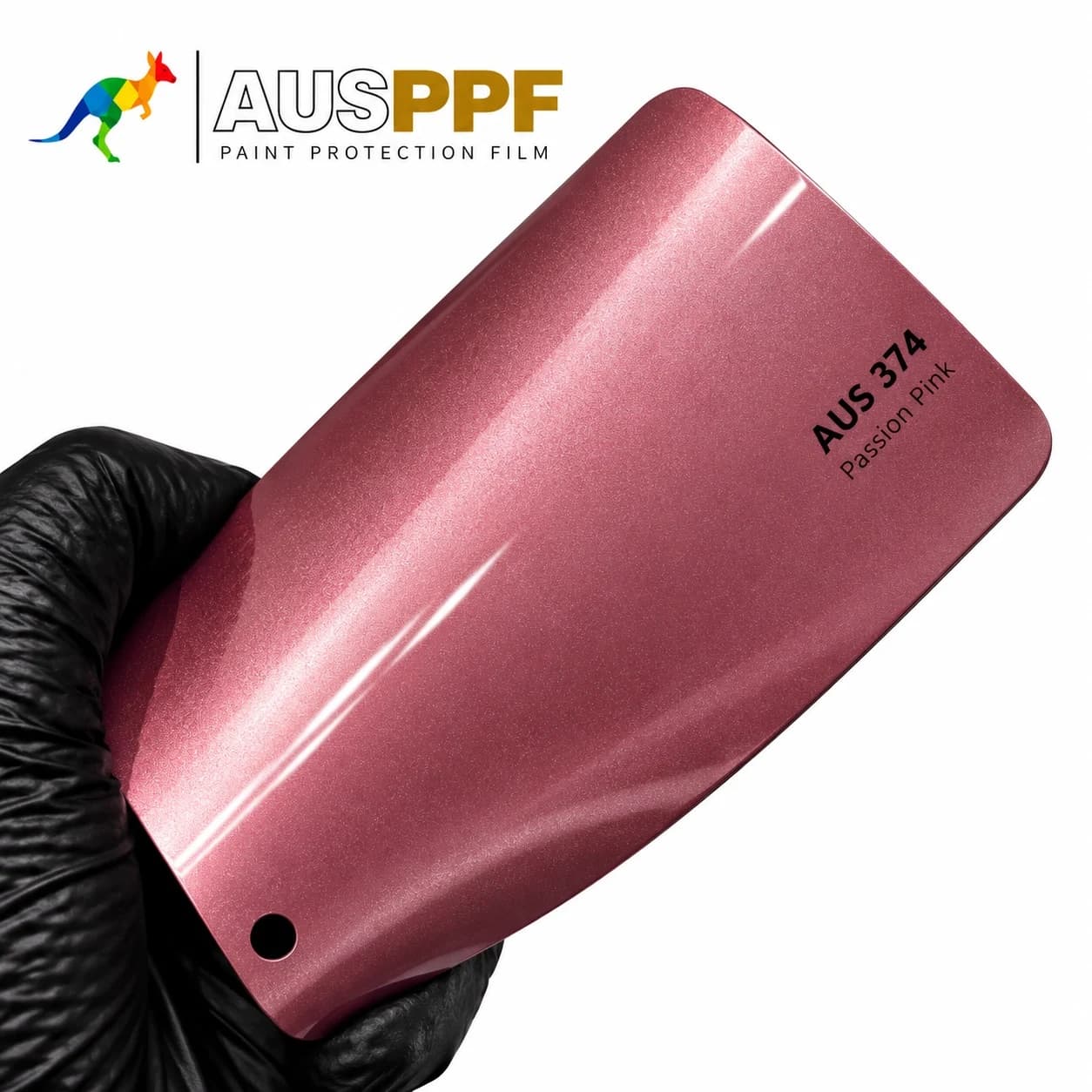 A gloved hand holding a swatch of AusPPF AUS-374 Passion Pink PPF, showing its gloss finish.