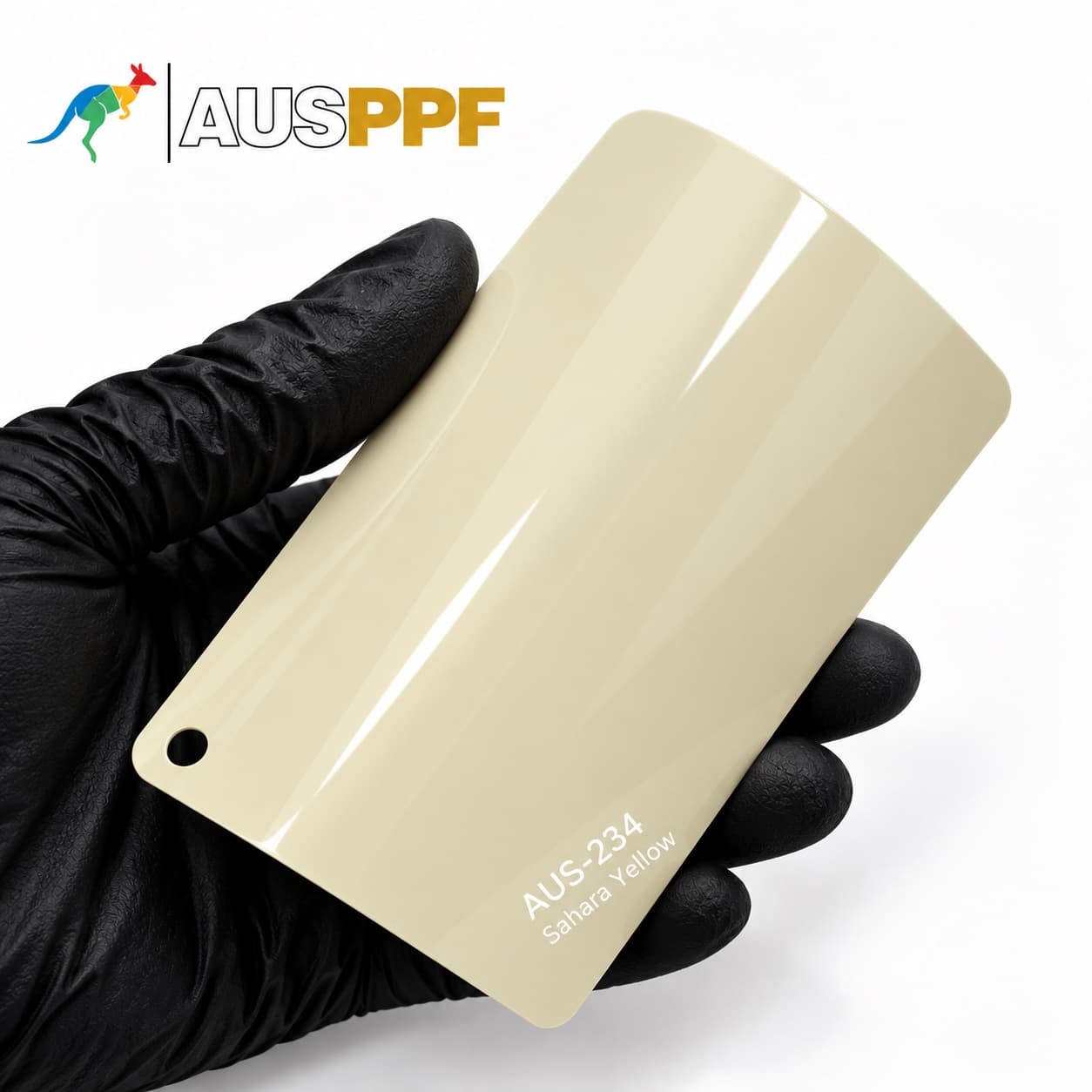 A gloved hand holding a swatch of AusPPF AUS-234 Sahara Yellow paint protection film, showing its warm creamy yellow finish.