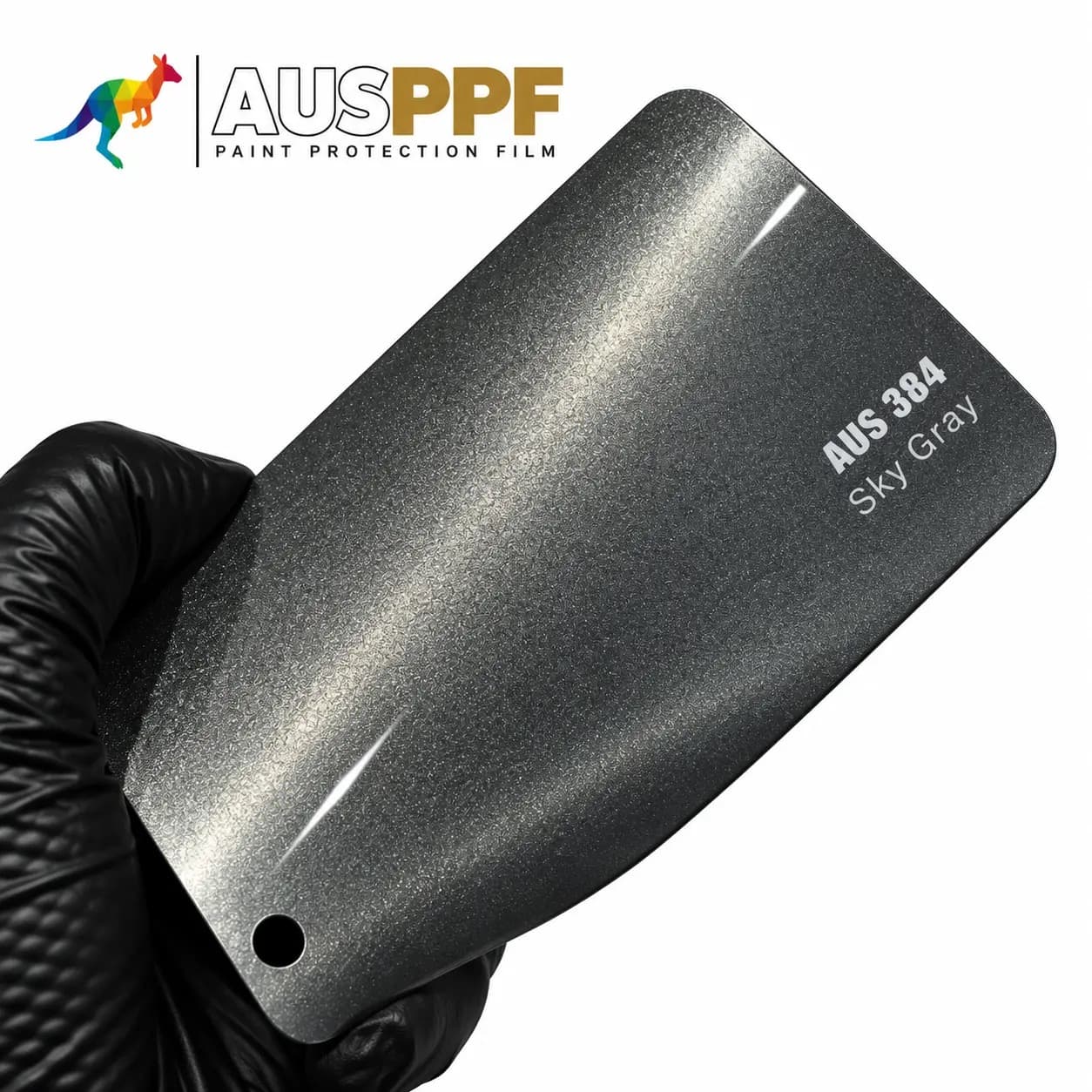 A gloved hand holding a swatch of AusPPF AUS-384 Sky Gray PPF, showing its gloss finish.