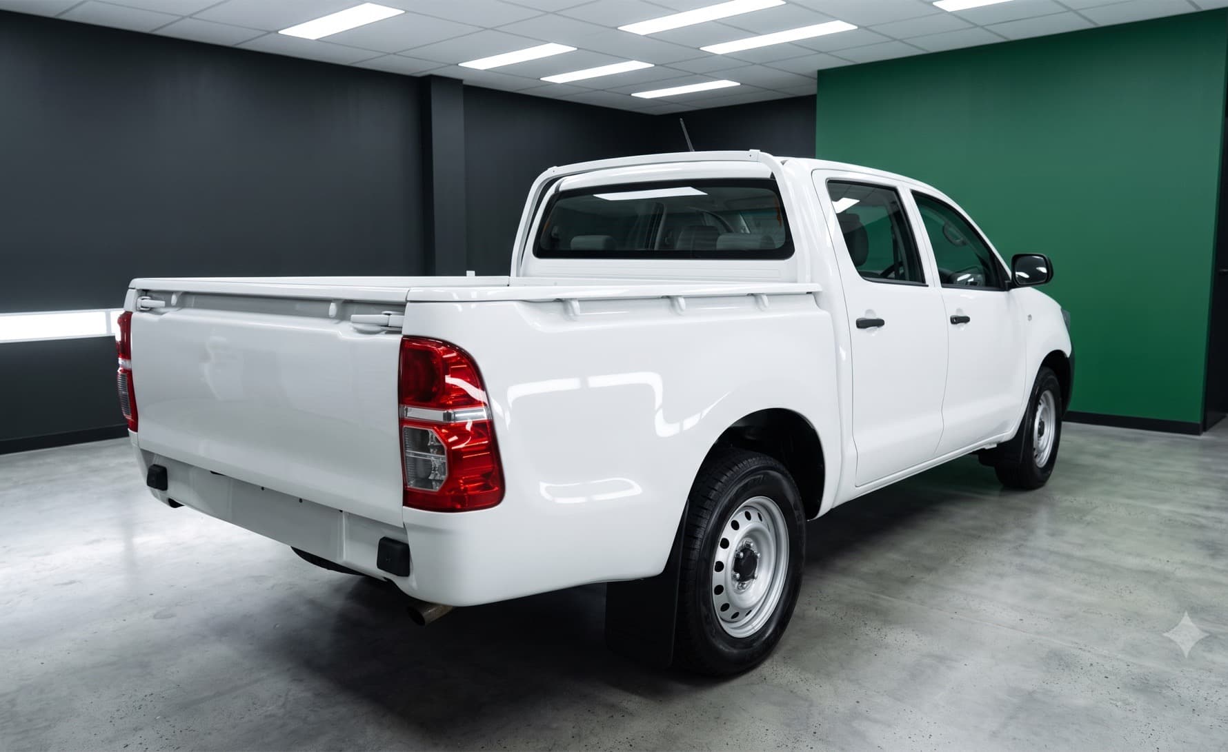 A white dual-cab ute in a workshop with dark grey walls and a green feature wall.